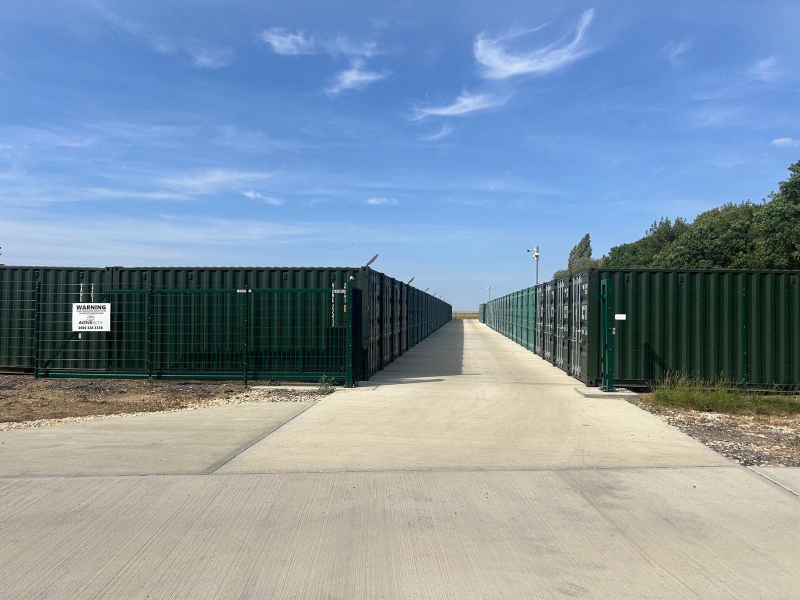 Wide concrete avenue running between two rows of green outdoor container storage units